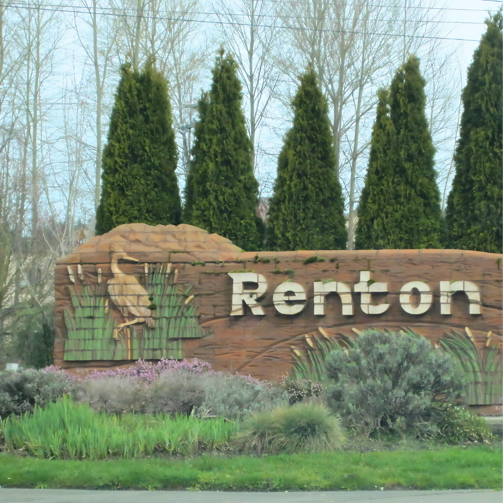 A landscaped wooden welcome sign for the City of Renton, Washington, featuring carved cattails and a heron motif surrounded by lush greenery—marking the entrance to a community where many people search for a dispensary near Renton.